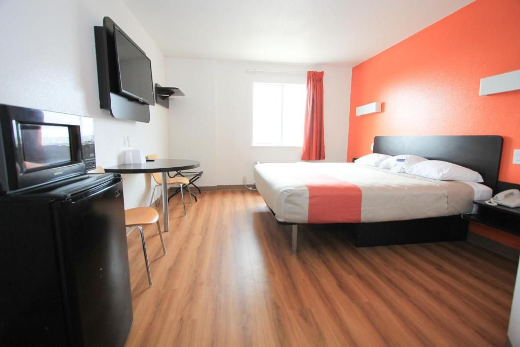 Una habitación de hotel con una cama, un escritorio con una silla, un televisor y una ventana con cortinas.