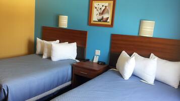 A hotel room with two beds, each with white bedding and a wooden headboard. There is a nightstand between the beds with a lamp and a telephone.