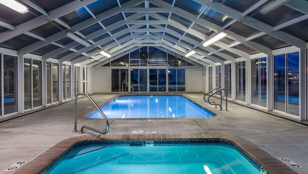 An indoor swimming pool with a high ceiling and glass walls, surrounded by a concrete floor and metal railings. - Days Inn by Wyndham Vernal (Vernal)