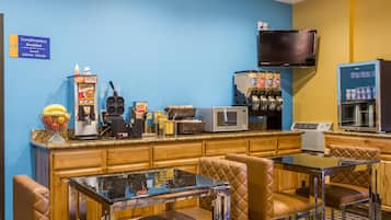 Een ontbijtbalk met zitplaatsen, een koffieapparaat, een magnetron en een aan de muur bevestigde televisie.