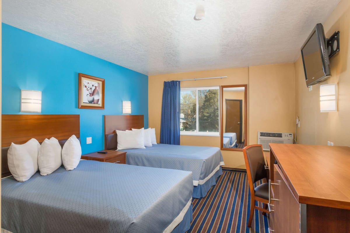 A hotel room with two beds, a desk, a television, and a window with curtains.