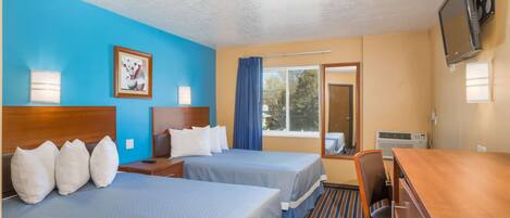 A hotel room with two beds, a desk, a television, and a window with curtains.