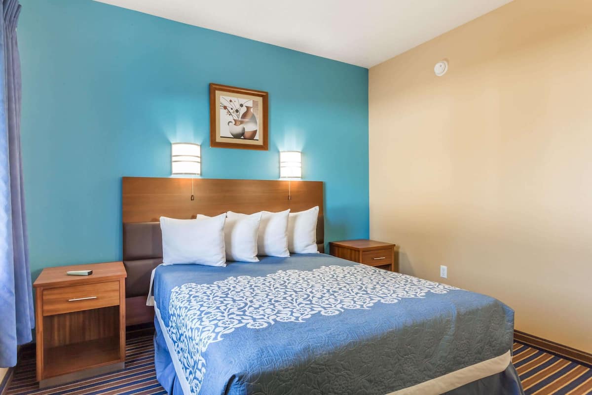 A hotel room with a large bed, two bedside tables, a headboard with wall-mounted lamps, and a framed picture above the bed.