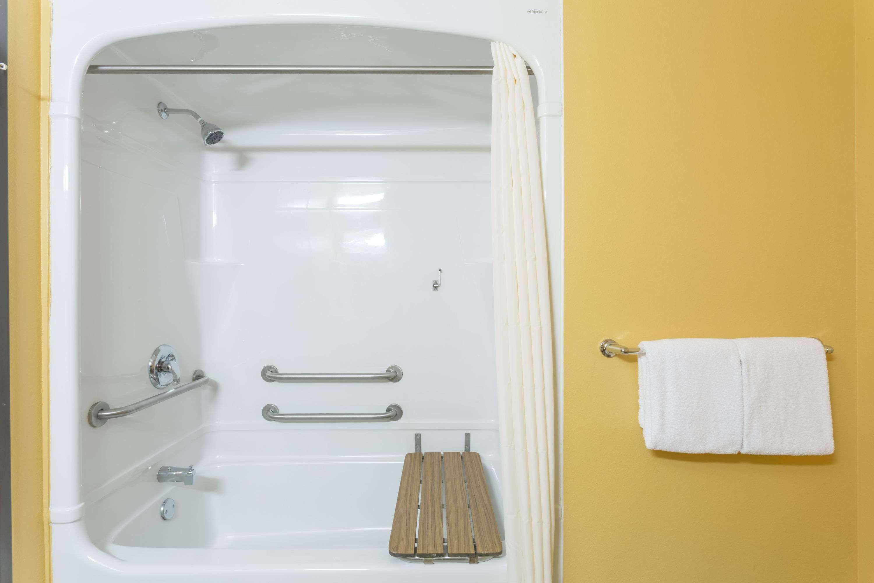 A bathroom with a bathtub, grab bars, a towel rack, and a wooden bath mat.