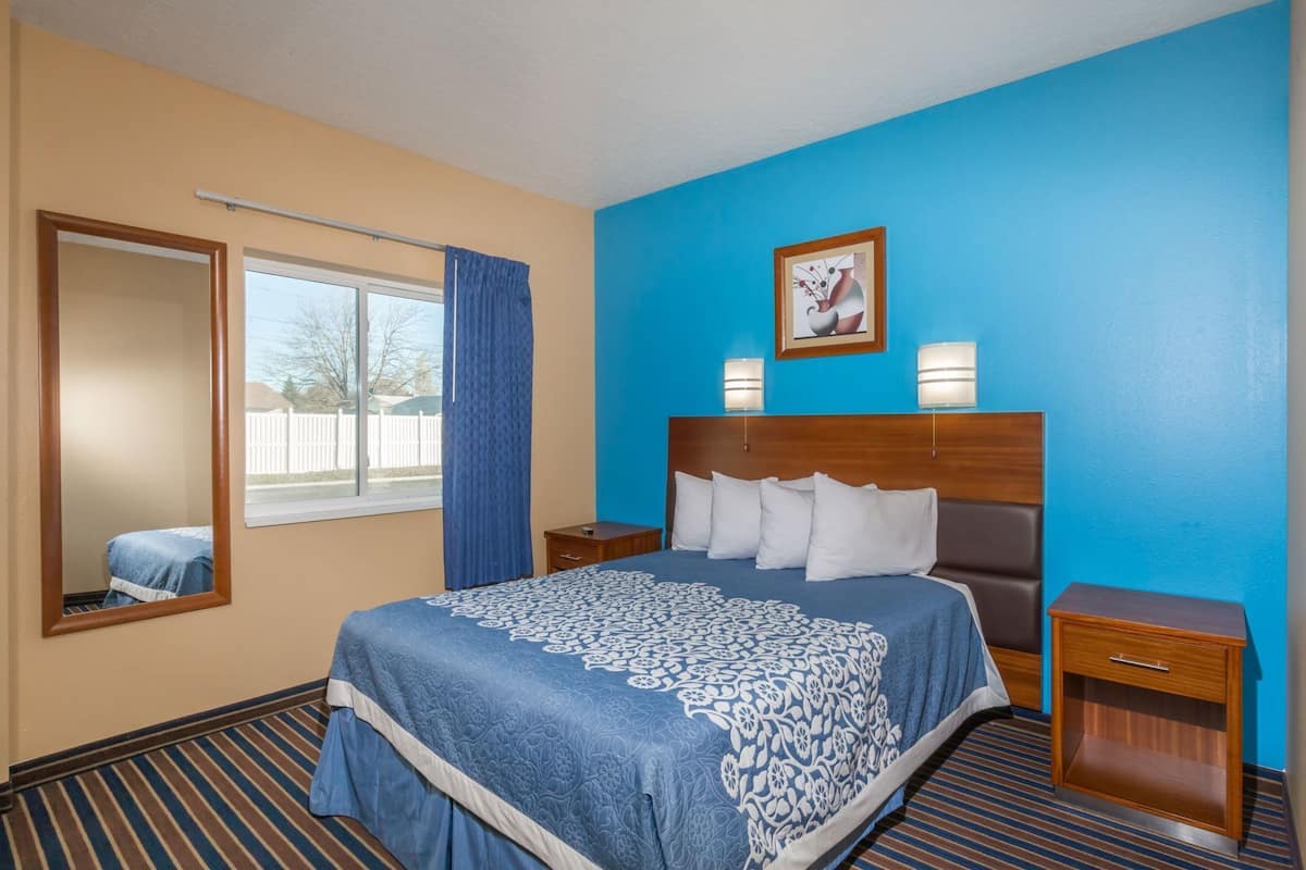 A hotel room with a large bed, a nightstand, a bedside table, a mirror, and a window with curtains.