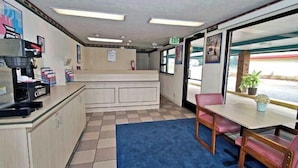 A reception area with a counter, a coffee station, a seating area with a table and chairs, and a view through the glass door. - Motel 6 Columbus, MS (Columbus)