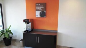 A coffee machine and a potted plant in a room with an orange accent wall. - Motel 6 Columbus, MS (Columbus)