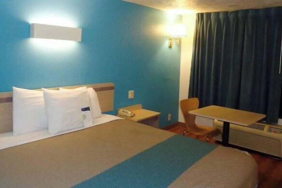 Une chambre d’hôtel équipée d’un lit, d’un bureau, d’une chaise, d’un téléphone et d’une fenêtre avec des rideaux.