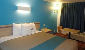 Une chambre d’hôtel équipée d’un lit, d’un bureau, d’une chaise, d’un téléphone et d’une fenêtre avec des rideaux.