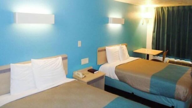 A hotel room with two beds, a small table, and a chair. - Motel 6 Columbus, MS (Columbus)