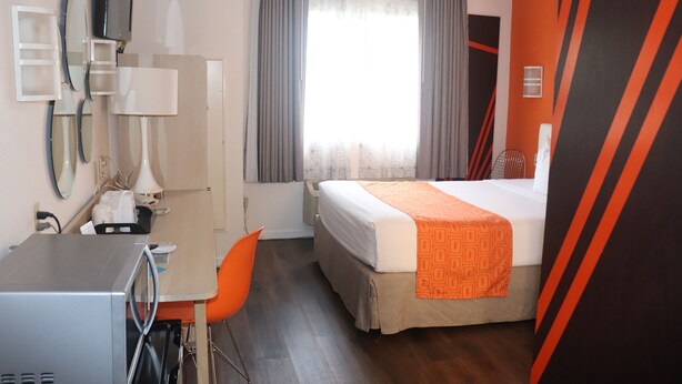 A hotel room with a bed, a desk with a chair, a microwave, a mirror, and a window with curtains. - Howard Johnson by Wyndham Tifton GA I-75 (Tifton)