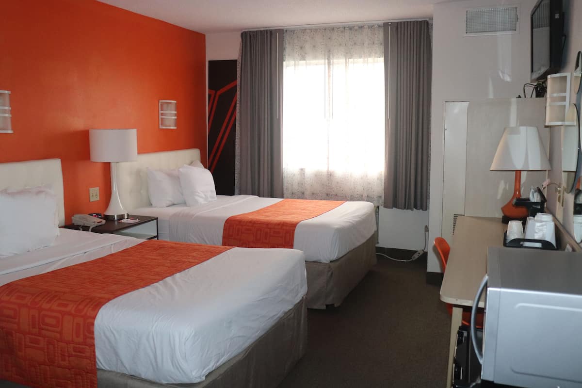 Quarto de hotel com duas camas, uma escrivaninha, uma cadeira, uma televisão e uma janela com cortinas.