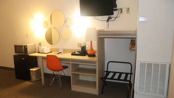 Una habitación de hotel con escritorio, silla, televisor, calentador y basurero.