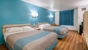 Hotellihuone, jossa on kaksi sänkyä, työpöytä, tuoli, ikkuna verhoilla ja pieni keittokomero.