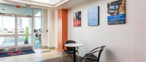 A hotel lobby with a reception desk, a glass door entrance, and a poster on the wall.