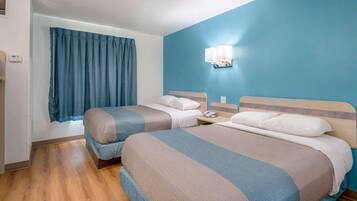 A hotel room with two beds, a blue wall, a window with curtains, and a bedside lamp.