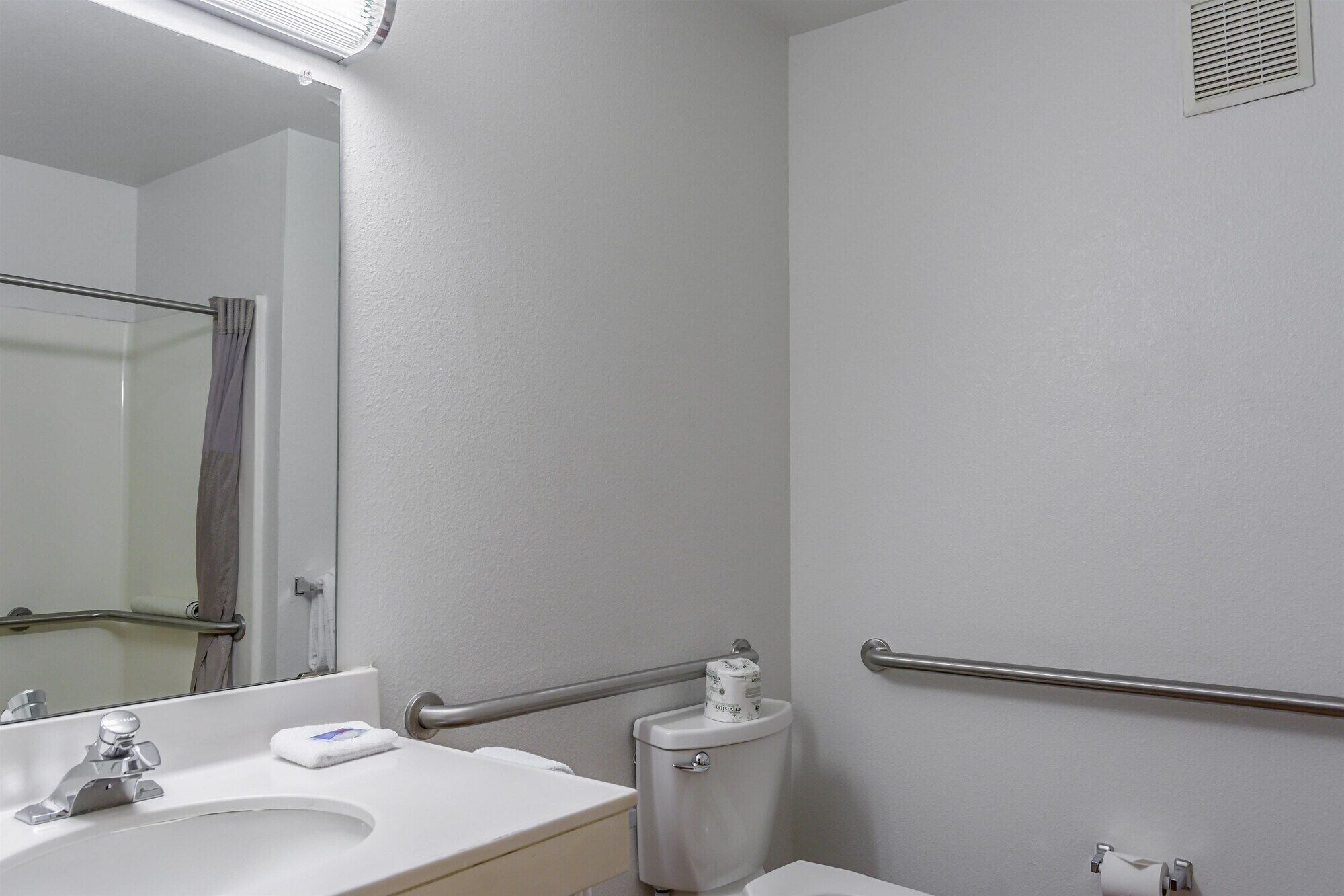 A bathroom with a white sink, mirror, toilet, and handrail.