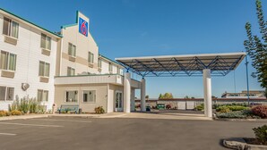 A motel with a covered parking area, a bench, and a landscaped garden. - Motel 6 Redmond, OR (Redmond)