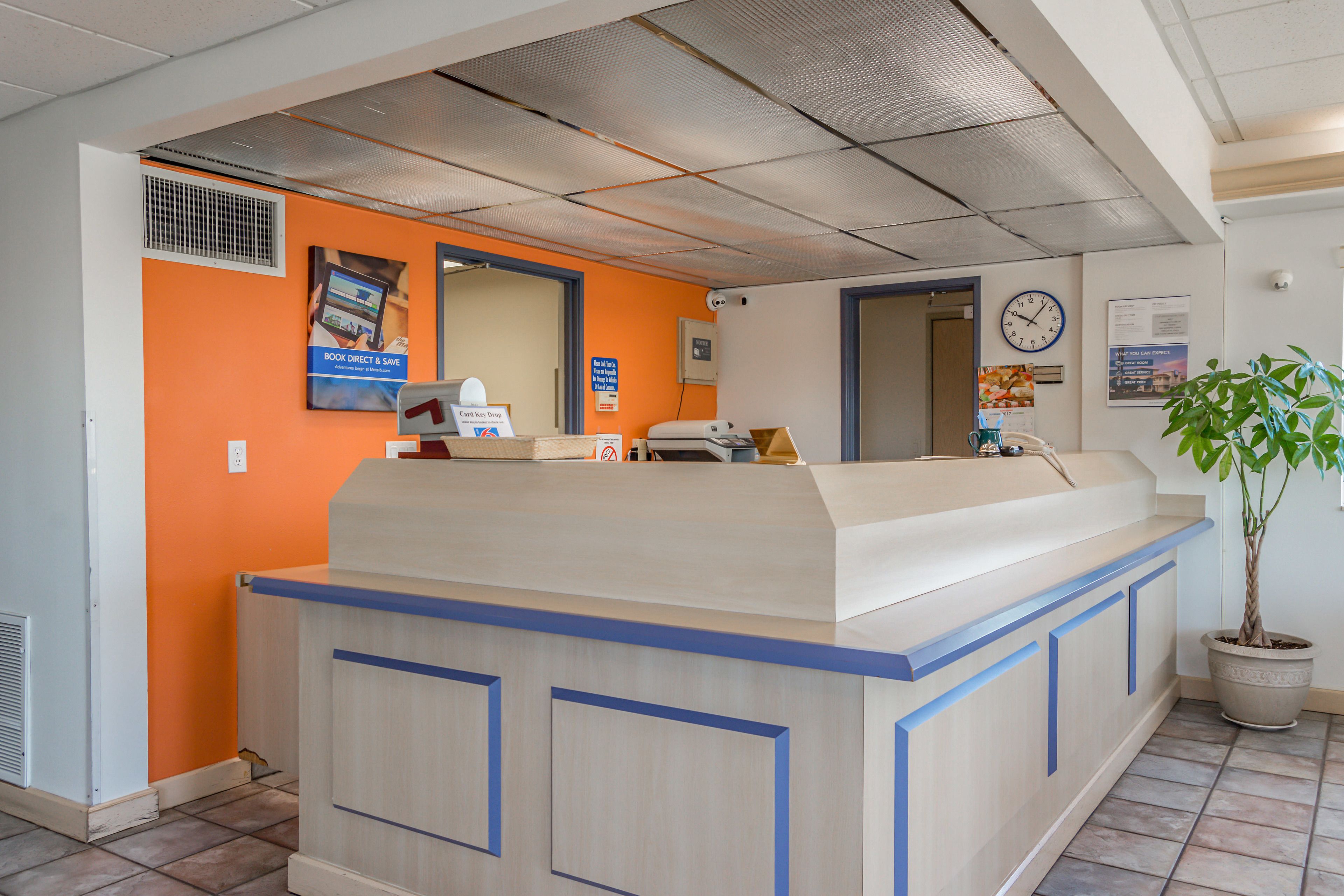 A reception desk with a light wood finish and blue accents, a potted plant, and a clock on the wall.