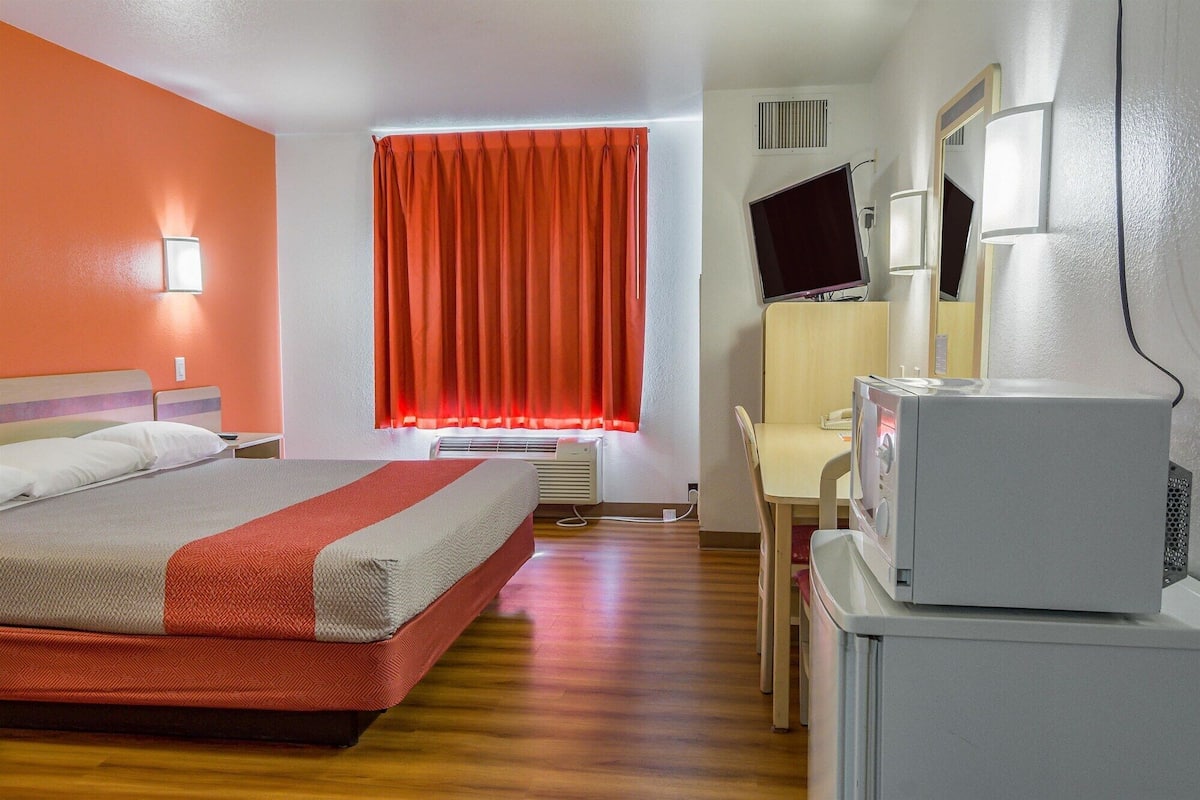 A hotel room with a bed, a desk, a television, and a window with curtains.