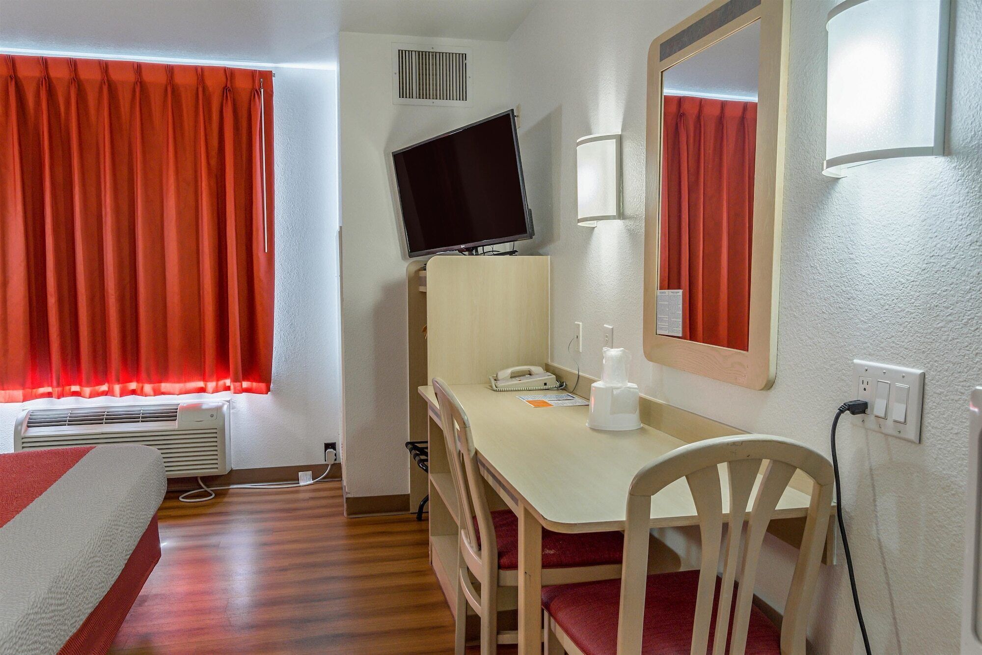 Habitación de hotel con escritorio, silla, televisor y cortinas rojas.