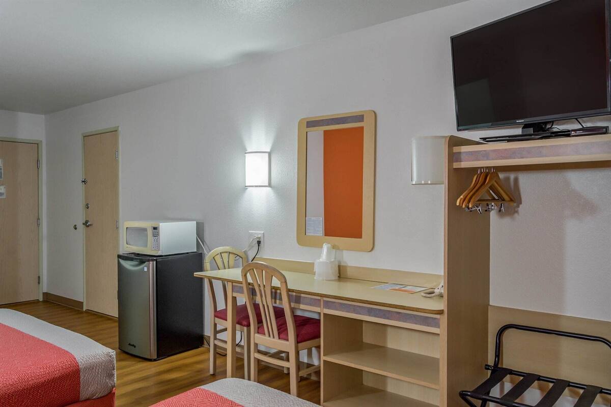 A hotel room with a bed, a desk with a chair, a television, a microwave, and a small refrigerator.