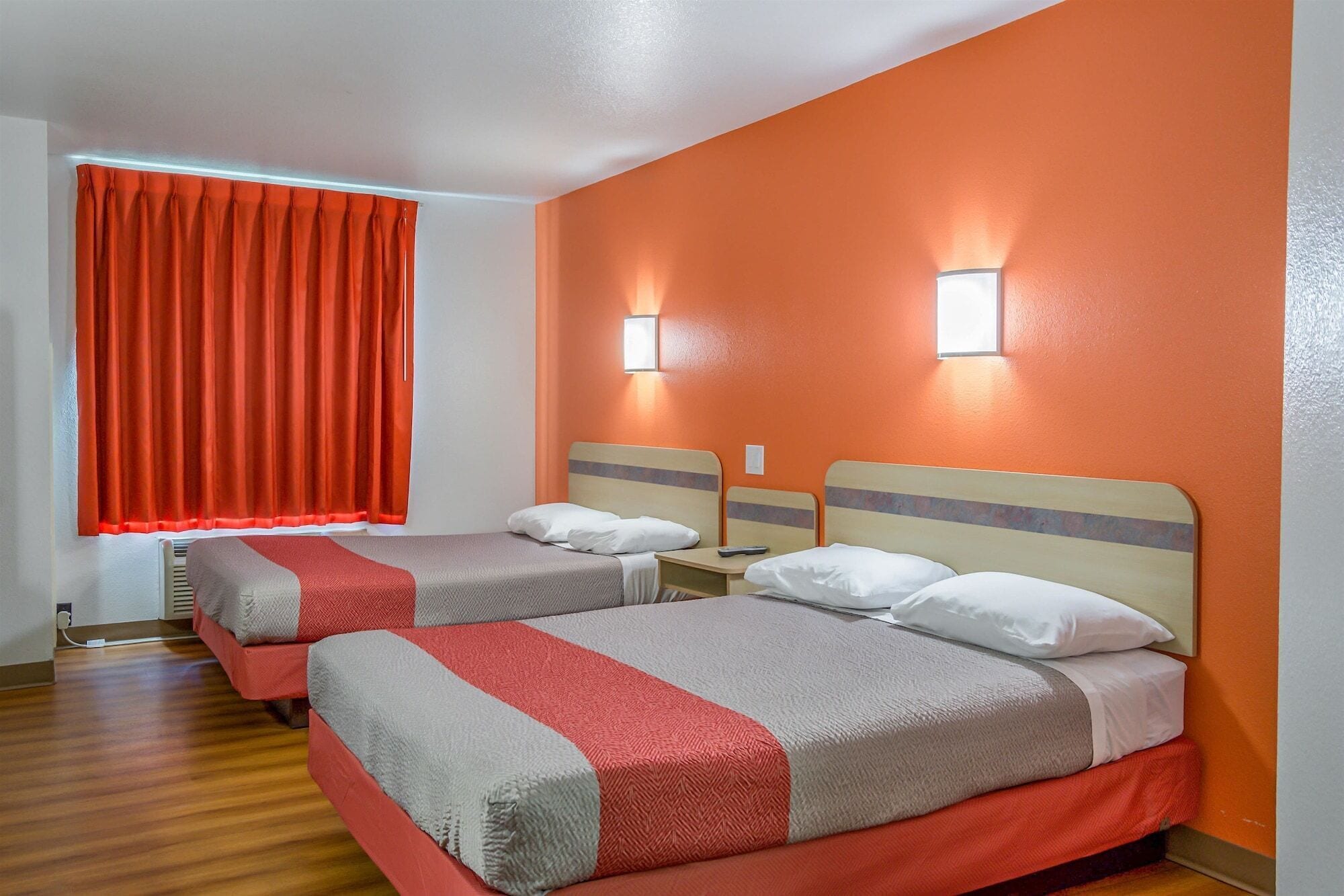A hotel room with two beds, orange walls, and a window with red curtains.