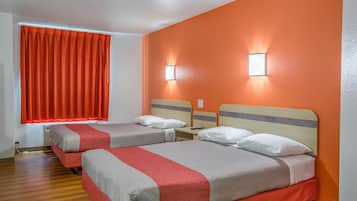 A hotel room with two beds, orange walls, and a window with red curtains.