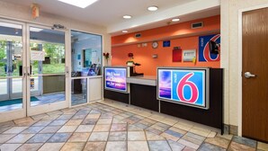 Un espace d’accueil avec un sol carrelé, un comptoir de réception, une horloge et un panneau indiquant « Motel 6 ».