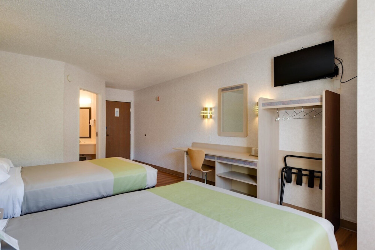 A hotel room with two beds, a desk, a chair, a mirror, a television, and a coat rack.