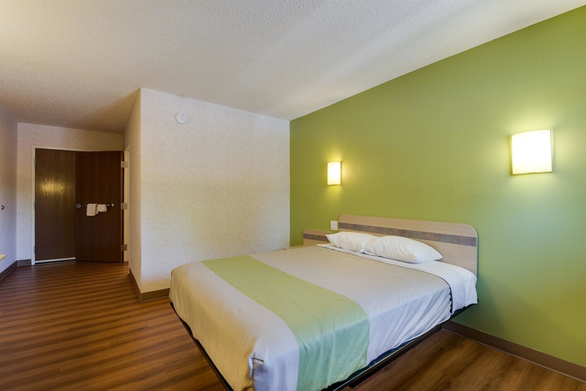A hotel room with a bed, wooden flooring, a green wall, and two wall-mounted lights.
