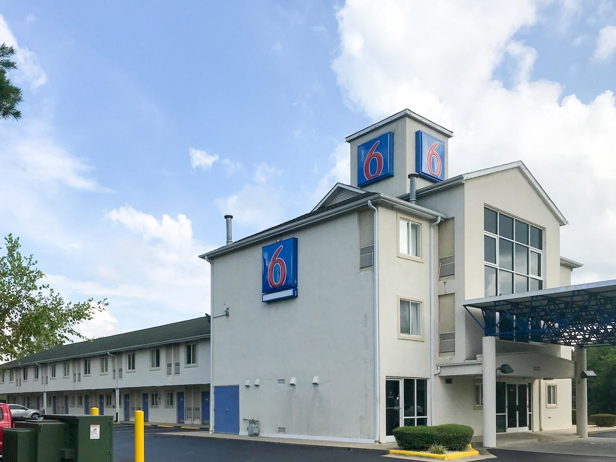A motel with a prominent '6' sign on the building, a covered entrance, and a parking lot with a green dumpster.
