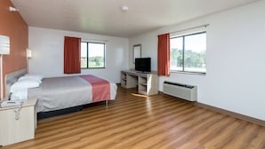 Ein Hotelzimmer mit Bett, Schreibtisch, Fernseher und großen Fenstern.