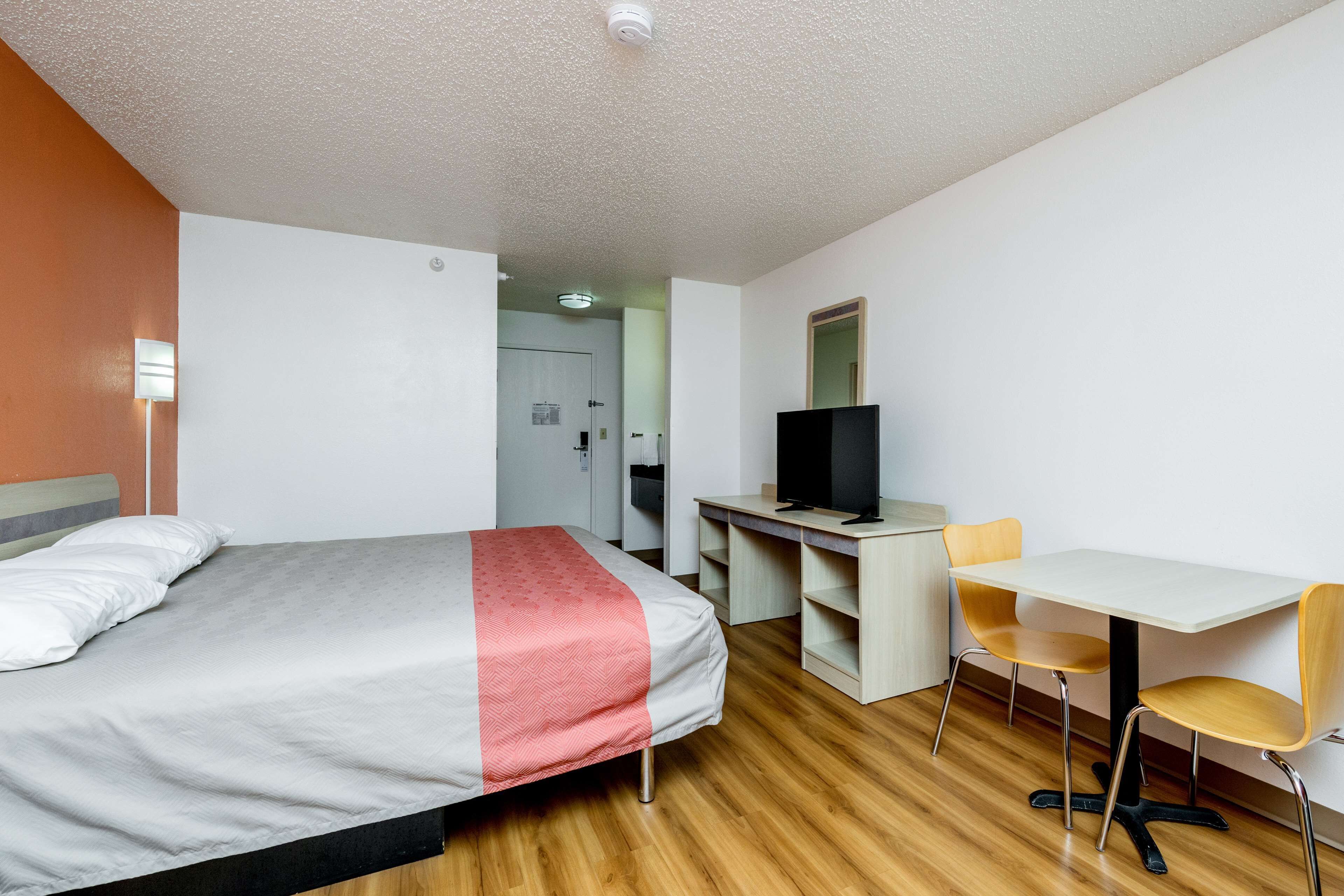A hotel room with a bed, desk, TV, and chairs.