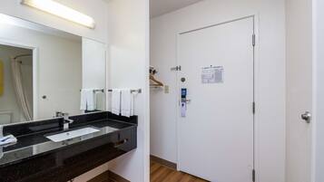 A hotel bathroom with a black countertop sink, a mirror, and a white door with a notice on it.
