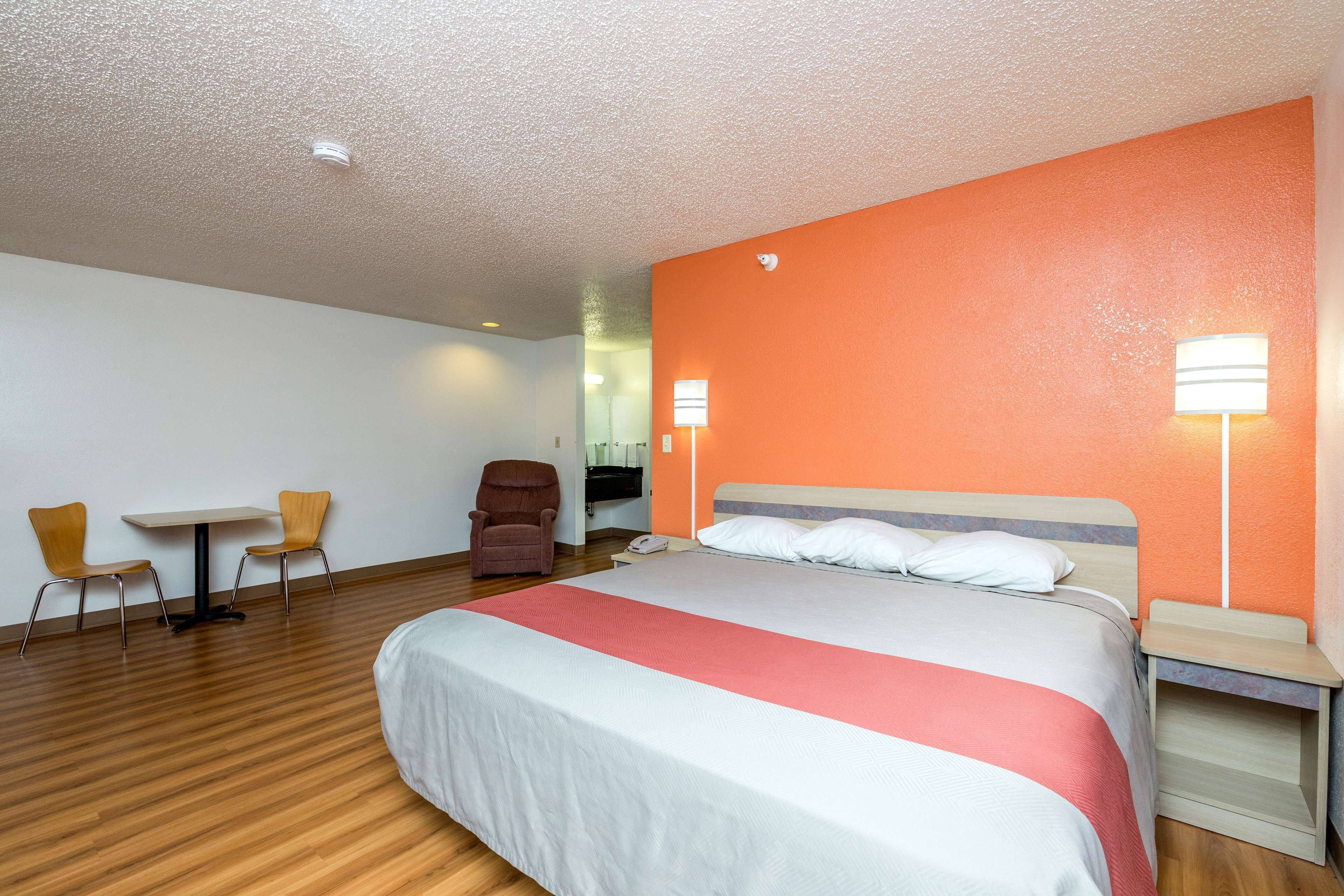 A hotel room with a large bed, two chairs, a small table, and a desk with a lamp.