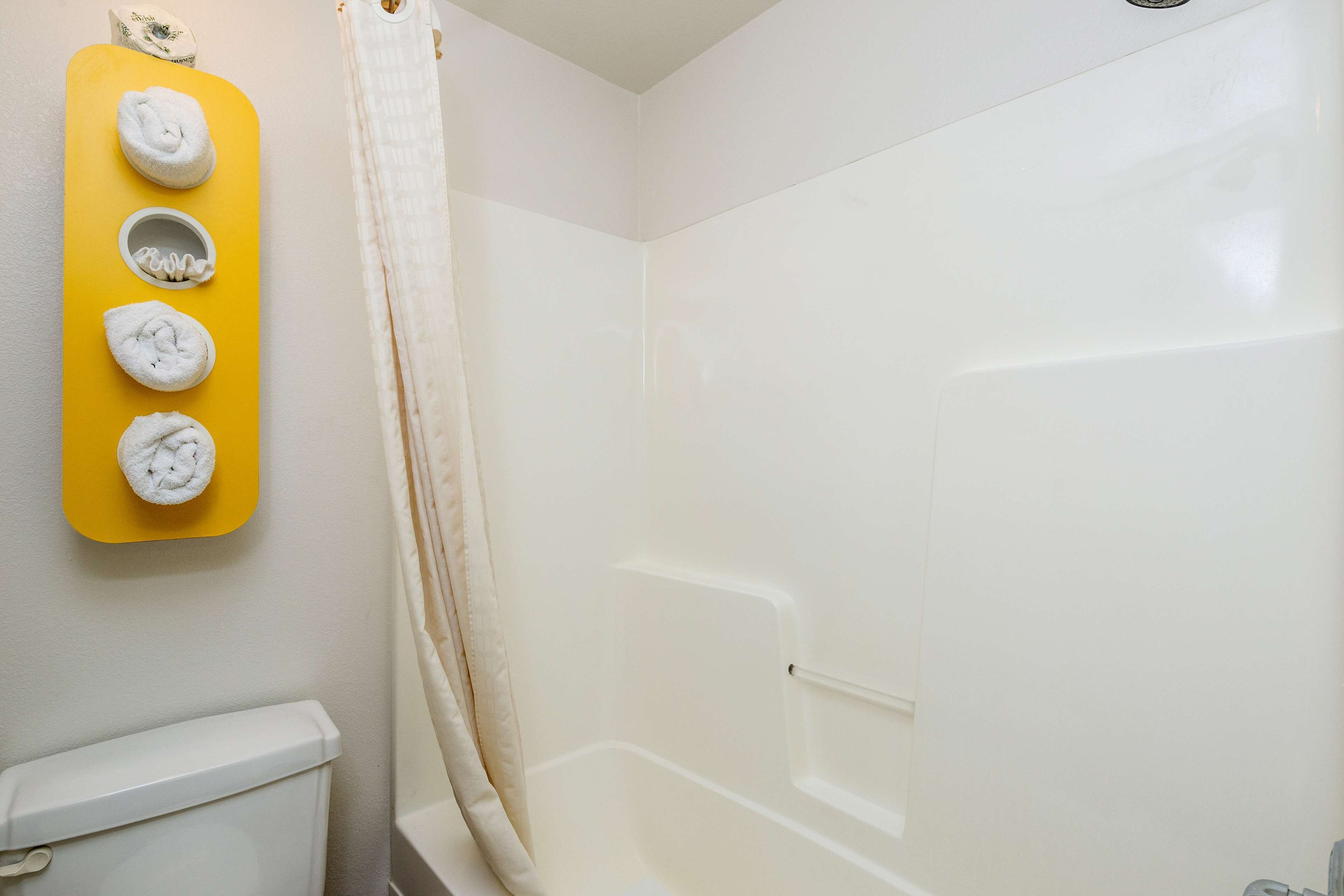 A bathroom with a white toilet, a yellow towel rack with four towels, and a bathtub.