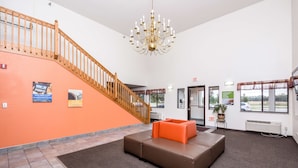 Eine Lobby mit Treppe, einer Kandelaber, einem braunen Sofa und einem kleinen Tisch mit Pflanze.