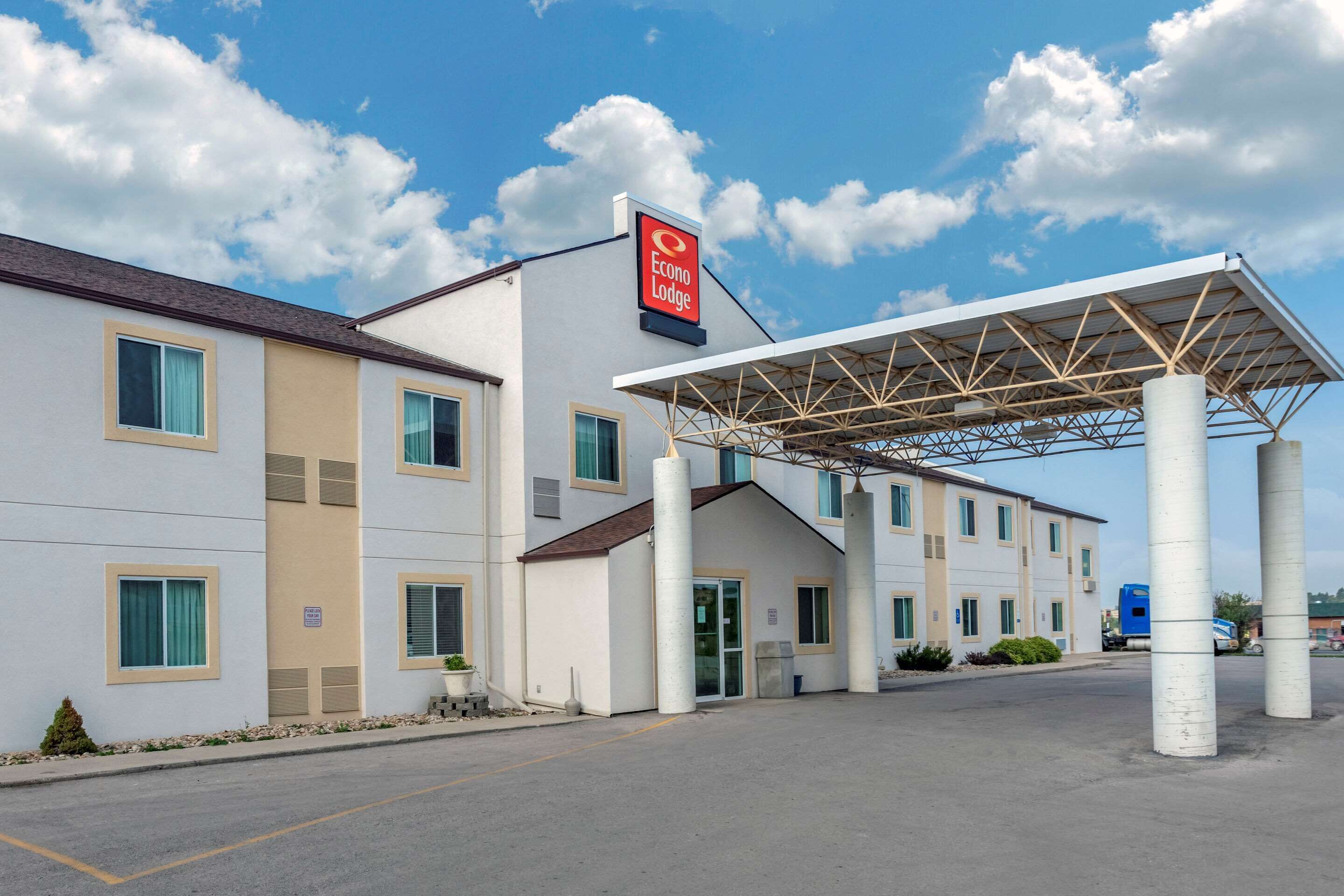 A hotel with a covered entrance, a prominent sign, and a parking lot.
