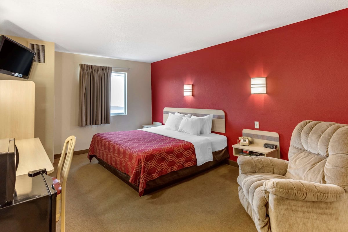 A hotel room with a bed, a desk, a chair, a TV, and two wall-mounted lights.
