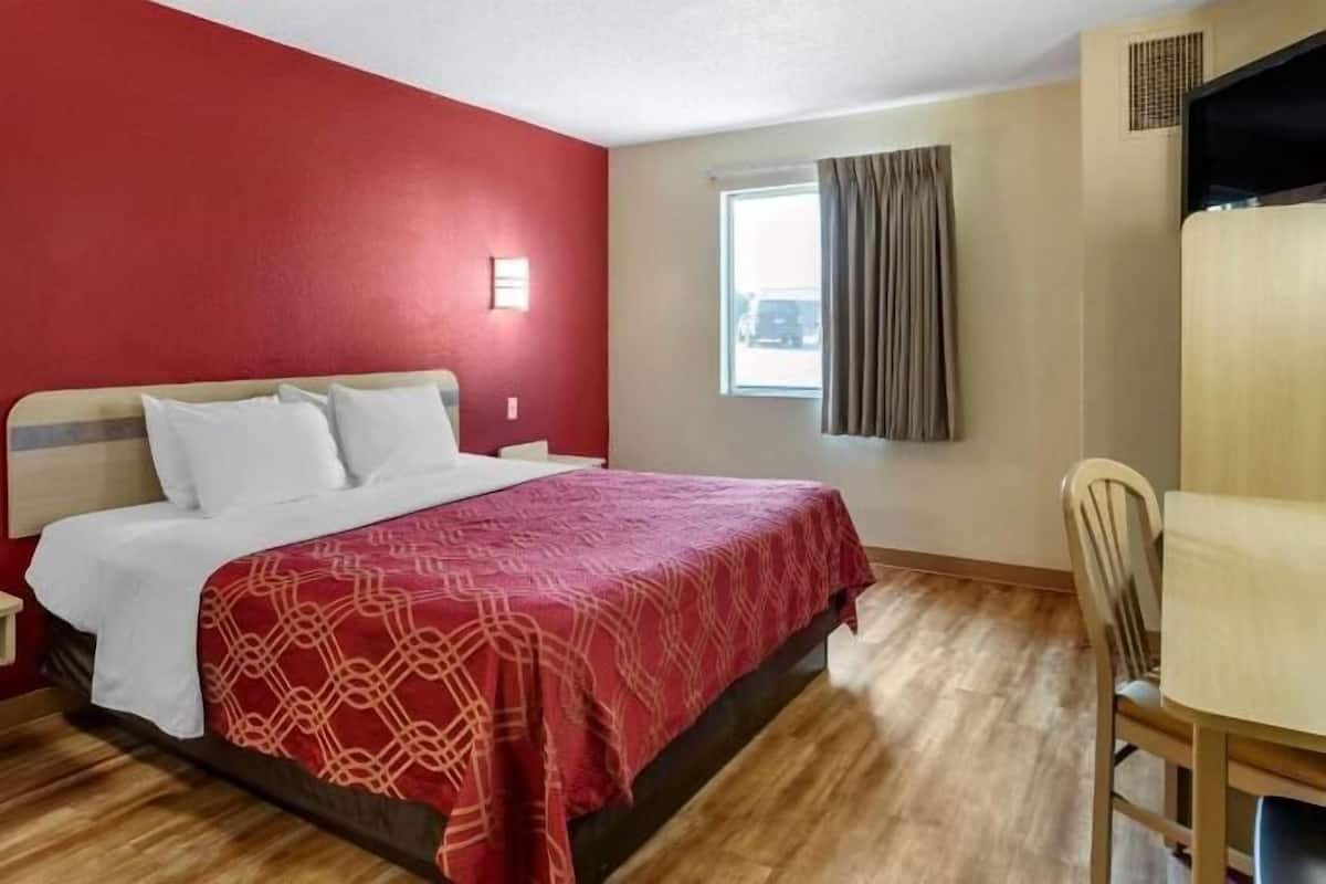 A hotel room with a bed, a desk, a chair, and a window with curtains.