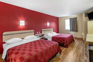 Habitación de hotel con dos camas, cada una con una colcha estampada roja, un cabecero de madera y una mesita de noche con lámpara.
