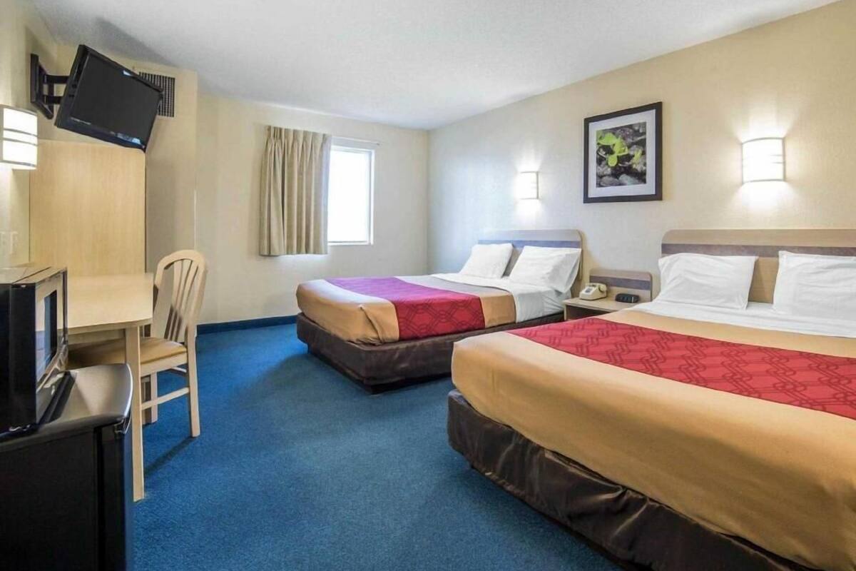 A hotel room with two beds, a desk, a chair, a TV, and a window with curtains.