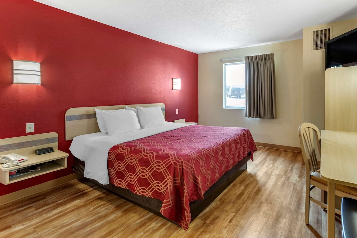 A hotel room with a bed, bedside table, lamp, and a window with curtains.
