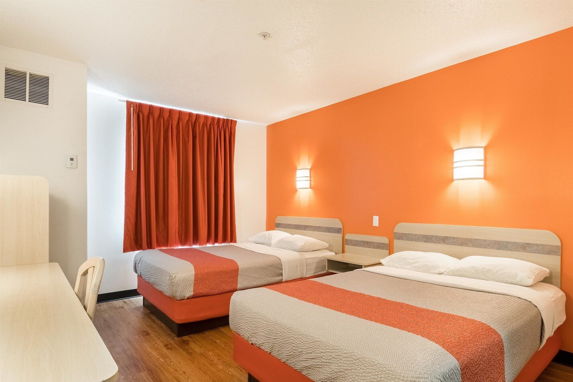 A hotel room with two beds, a dining table, and orange walls.