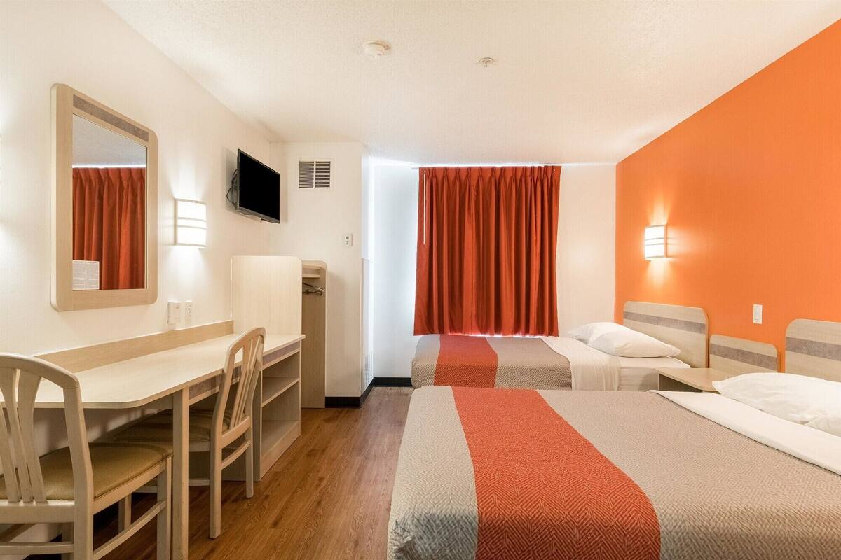 A hotel room with a desk, two beds, a television, and a shower area.