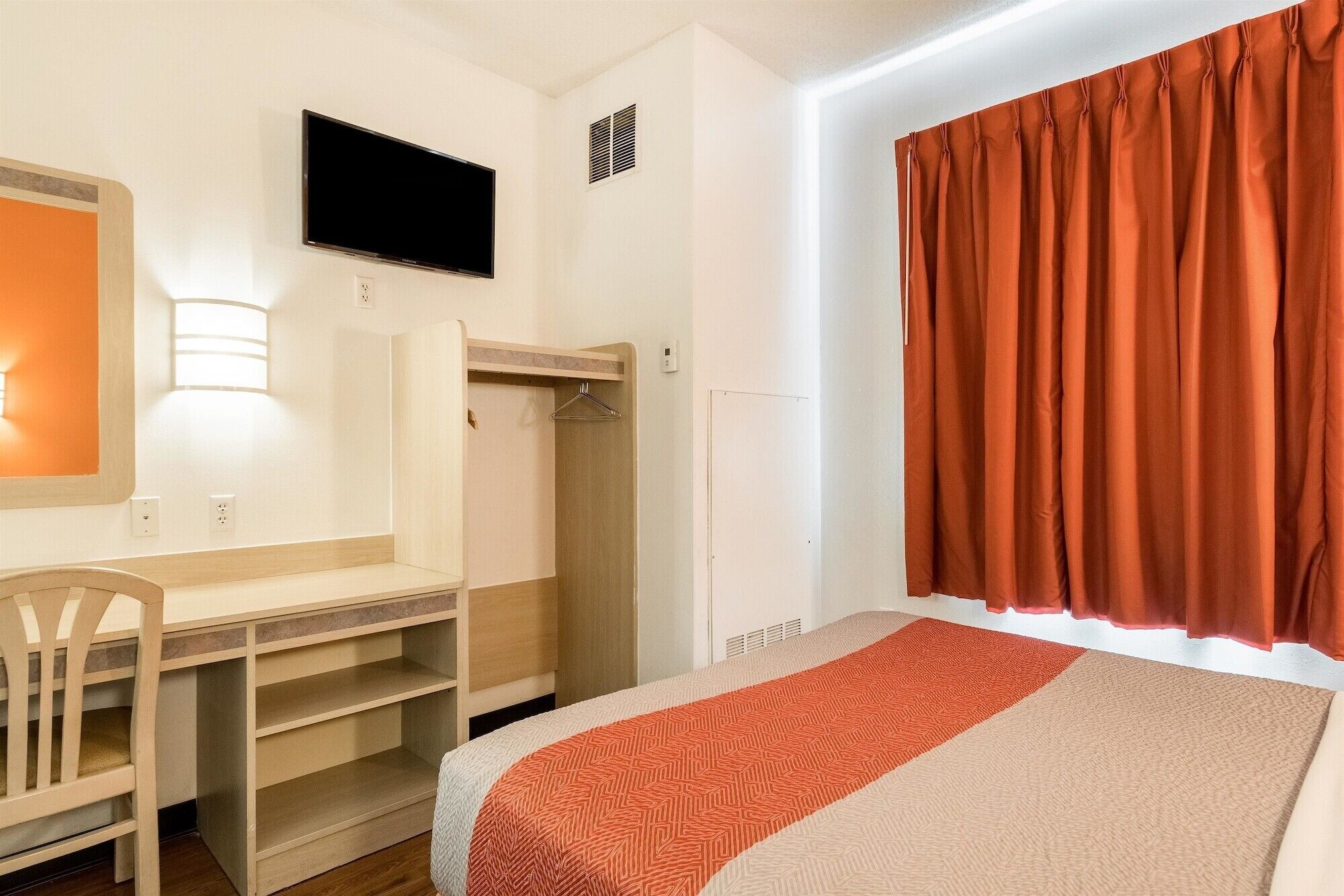 Een slaapkamer met een bed, een bureau, een stoel, een kledingkast, een televisie en een raam met gordijnen.