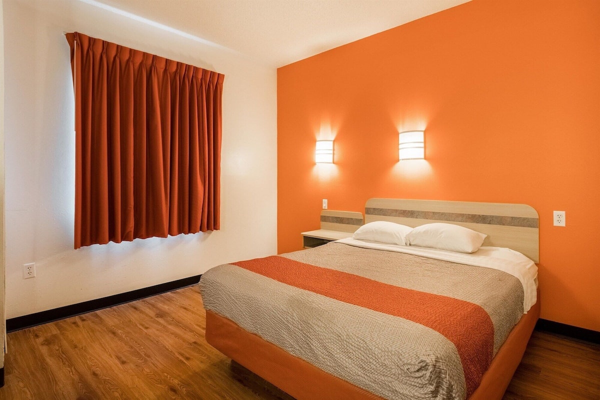 A hotel room with a bed, a window with curtains, and two wall-mounted lights.