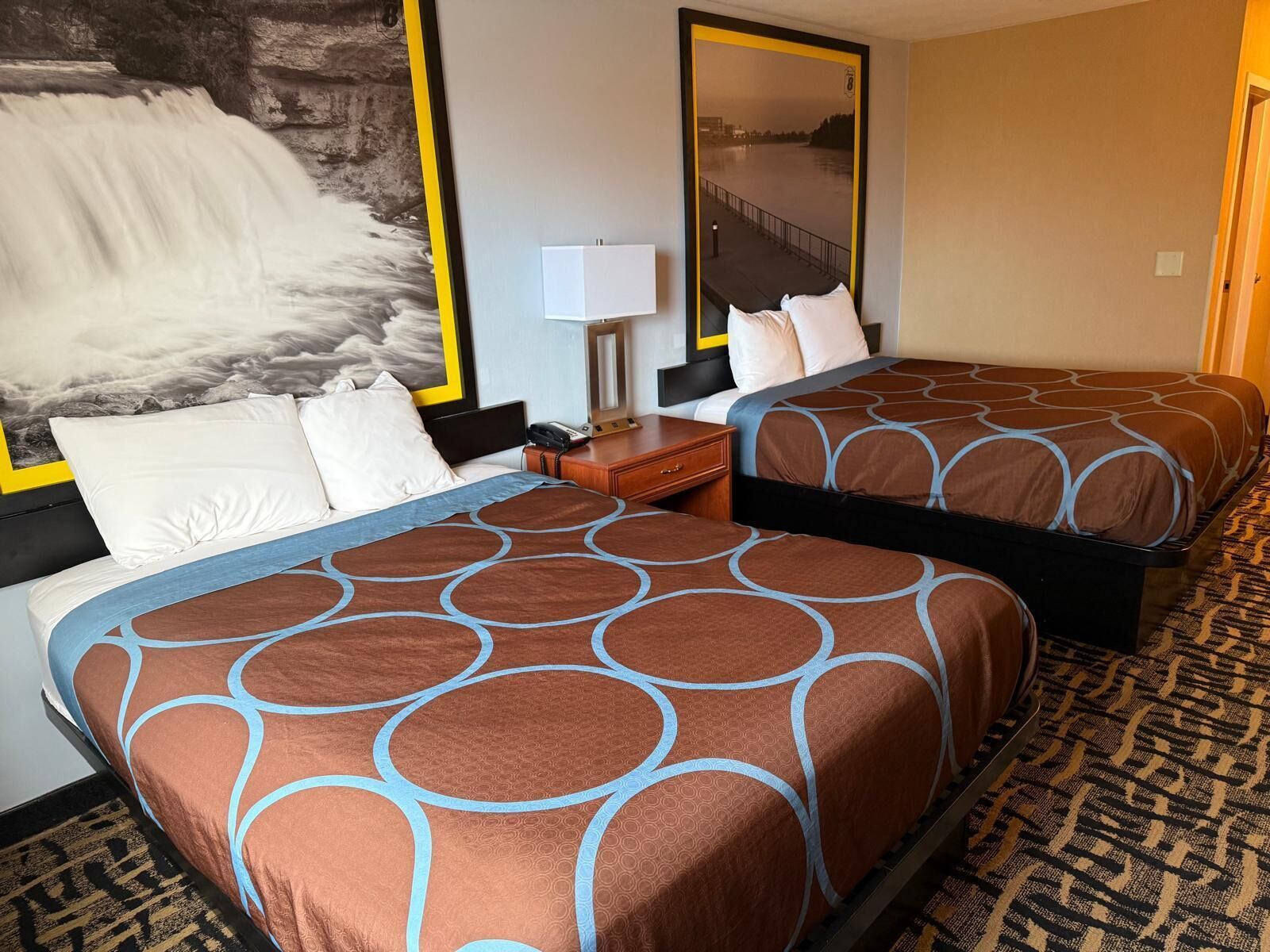 A hotel room with two beds, a large mirror, a nightstand, and a view of a river.