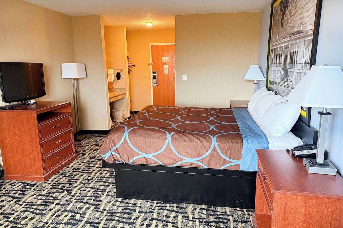 Ein Hotelzimmer mit Bett, Fernseher, Schreibtisch und einem durchgegangenen Tür erkennbaren Badezimmer.